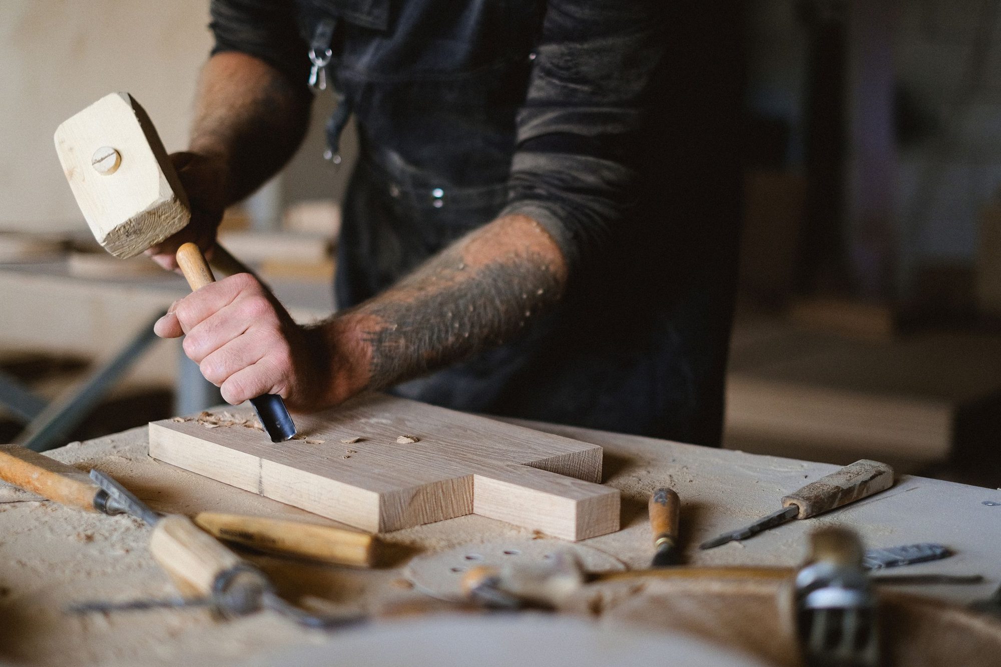 Nahaufnahme: Ein Tischler treibt mit einem Holzhammer einen Stechbeitel ins Holz.